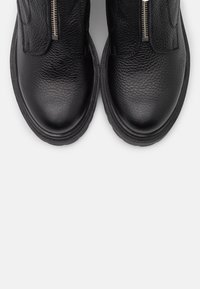 Bottes chevilles en cuir noir à surface texturée, avec une fermeture éclair latérale et un bout arrondi, sur fond blanc.