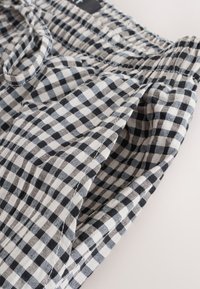 Shorts med gingham-mønster i sort og hvid, med elastisk talje og snøre. Stoffet virker let og tekstureret.