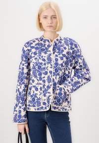 Floral-patterned jacket in cream and blue, featuring long sleeves, a round neckline, and two front pockets. Smooth fabric texture.