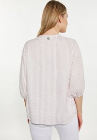 Lett bluse i pastelfarvet stribet stof med langt halvmånedsærmer og rund bund, der har en lille knapdetalje bagpå.