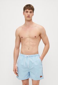 Bañador azul claro con una cintura elástica y cordón ajustable, que presenta franjas laterales y un pequeño parche de logo. Textura de tela suave.