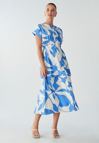 Plava i bijela haljina s uzorkom, kratkim rukavima, dugmadi sprijeda, elastičnim strukom i lepršavom suknjom. Tkanina izgleda lagano i teksturirano.