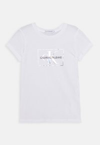 Bílý bavlněný tričko s kulatým výstřihem, na kterém je velké černé obdélníkové logo s nápisem "CALVIN KLEIN JEANS" a zrcadlovými akcenty.