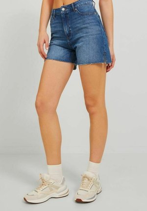 Shorts de mezclilla de talle alto en azul oscuro, con un dobladillo deshilachado, dos bolsillos frontales y una textura suave, combinados con zapatillas en tonos neutros.