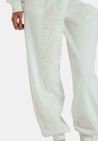 Pantalones de chándal blancos con un patrón de hojas texturizado y con lentejuelas que recorre el lado exterior, con un corte holgado y puños elásticos.