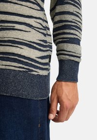 Maglione lavorato a maglia navy e beige con motivo a strisce testurizzate, polsini e orlo a coste, dotato di una piccola etichetta del marchio sul lato.