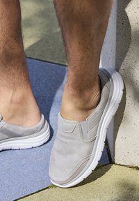 Gray slip-on shoes made of suede with a cushioned sole, featuring a white rubber outsole and red stitching detail along the front.