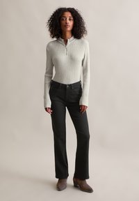 Haut à manches longues rayé gris clair avec un col zippé, associé à un jean noir à jambes droites et des bottines à talons marron. Design simple et ajusté.