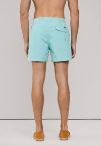 Costumi da bagno a righe turchesi con vita elastica, tasca posteriore e lunghezza corta, realizzati in tessuto leggero.