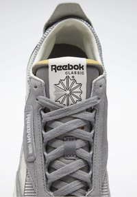 Baskets Reebok Classic grises avec détails en mesh et en suède, lacets croisés, et étiquettes de marque sur la languette et le côté.