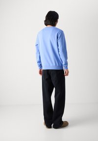 Felpa blu realizzata in morbido tessuto, con colletto girocollo e maniche lunghe, abbinata a jeans dritti scuri e scarpe marroni.