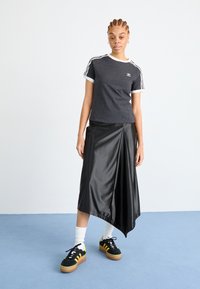 Zwarte satijnen asymmetrische rok gecombineerd met een grijze T-shirt met witte randen en drie witte strepen op de mouwen, aangevuld met zwarte sneakers.