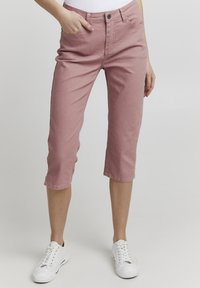 Pantalones cortos de mezclilla en color rosa claro, con cintura ajustada, bolsillos delanteros y dobladillos enrollados, combinados con zapatillas blancas.