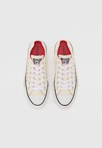 Beige vászon sportcipők fehér fűzővel, fekete részletekkel és zöld eper mintázattal. Piros belső bélés "Converse All Star" logóval.