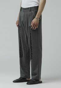 Gray plaid trousers feature black floral embroidery on the sides, with a relaxed fit and a belt loop for added detail. Smooth fabric texture.