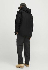 Svart isolerad jacka med huva, bärs över mörka cargobyxor. Har en avslappnad passform och fickor. Beige skor kompletterar outfiten.