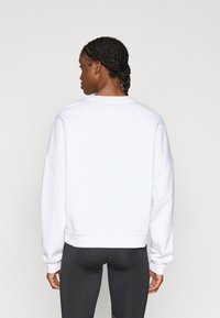 Λευκό φαρδύ φούτερ με στρογγυλή λαιμόκοψη και χαλαρούς ώμους. Λεία υφή και ριγέ μανσέτες. Φορεμένο με μαύρο στενό κολάν.