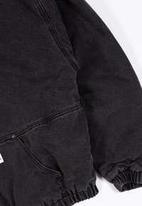 Juodas džinsinis švarkas su tekstūru, elastinėmis rankovėmis ir priekinėmis kišenėmis. Minimalistinis dizainas su sustiprintais siuvimo detalėmis.