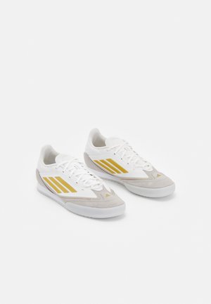 Weiße und beige Sportschuhe mit goldenen Streifen, ausgestattet mit einer glatten matten Oberfläche, strukturierten Wildlederakzenten und einem Schnürdesign.