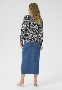 Top w leoparda, z długimi rękawami, w połączeniu z dżinsową spódnicą maxi. Spódnica jest niebieska, prosta, z tylnymi kieszeniami i teksturowanym wykończeniem.