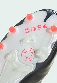 Semelle de crampons de football noire avec design transparent, crampons roses et logo "COPA" en rose vif. Présente des rainures texturées pour l'adhérence.