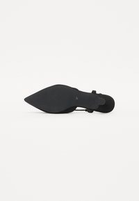 Zapato de tacón alto de ante negro con punta afilada y suela negra lisa. Presenta una delgada correa en el tobillo y una textura sutil en la superficie.
