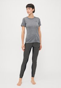 Szürke, rövid ujjú póló, kerek nyakkivágással, fekete leggings-el kombinálva, amelyeken fehér geometrikus minta és oldalsó panelek találhatók.