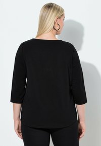 Schwarzes Dreiviertelarm-Oberteil aus weichem Stoff mit rundem Ausschnitt und leicht geschwungenem Saum hinten. Einfaches, minimalistisches Design.