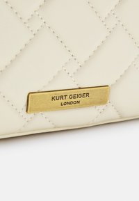 Portafoglio in pelle trapuntata crema con una targhetta in metallo dorato recante la scritta "Kurt Geiger London". I dettagli cuciti esaltano il design.