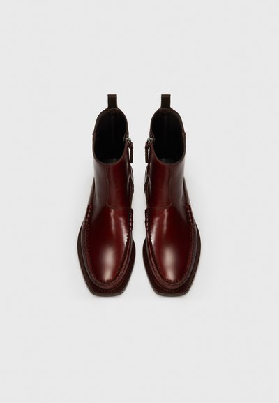 Bottines en cuir bordeaux avec un design épuré, des fermetures éclair sur les côtés et une semelle en caoutchouc marron contrastante. Caractéristiques de détails cousus le long des bords.