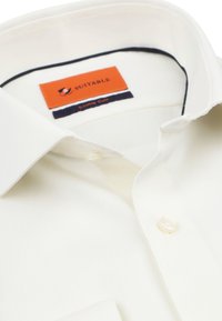 Lichtcrème overhemd van zachte stof. Kenmerken zijn een klassieke kraag, een enkele knoopmanchet en een oranje label met 'Suitable - Double Cuff.'