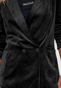 Blazer nero doppiopetto in tessuto morbido e strutturato con due bottoni e tasche laterali. Presenta un design con rever a punta.