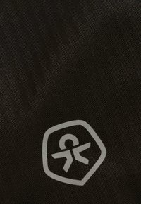 Tmavá tkanina s jemným herringbone vzorom obsahuje malý, svetlosivý abstraktný symbol vo vnútri hexagonu blízko pravého dolného rohu.