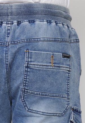 Hellblaue Denim-Jogginghosen mit elastischem Bund, ausgestattet mit einer Gesäßtasche und gelben Nähten. Markenlabel auf der Tasche angebracht.