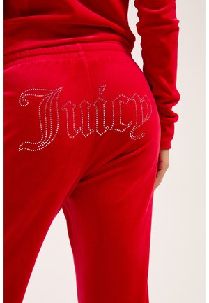 Pantalon en velours rouge avec le mot "Juicy" écrit en strass sur la zone de la poche arrière, porté avec un haut rouge assorti.