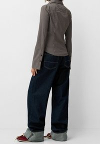 Raidallinen nappikauluspaita pitkillä hihoilla, istuva malli ja kaulus, yhdistettynä väljään tummansinisestä denimpäällyksestä valmistettuihin farkkuihin, joissa on käärityt lahkeet.