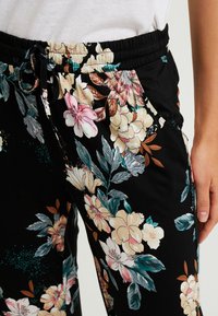 Zwarte bloemenbroek met een verscheidenheid aan pastelbloemen en bladeren, met een elastische tailleband en koord. Zachte, lichtgewicht stof.