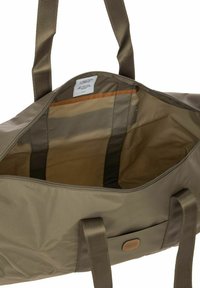 Sac de sport vert olive avec un extérieur en nylon lisse, fermeture éclair et accents beige. Intérieur spacieux avec une poche zippée et doublure en tissu.