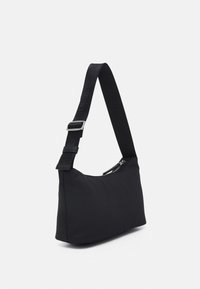 Musta, pehmeä kangaskäsilaukku vetoketjukiinnityksellä. Varustettu säädettävällä hihnalla, jossa on teksturoitua mustaa metallia. Kompakti, minimalistinen muotoilu.