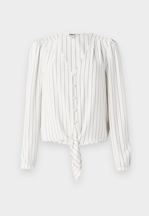 Blusa bianca a maniche lunghe con righe verticali nere, presenta un colletto a V, chiusura con bottoni e un orlo anteriore annodato. Tessuto dalla texture liscia.