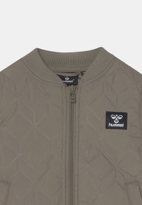 Steppjacke im olivgrünen Farbton mit Rippenkragen, Reißverschluss und einem schwarzen Markenlogo-Patch auf der linken Brust.