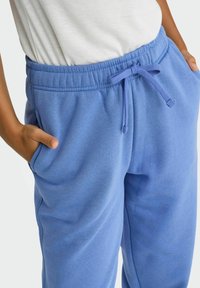 Blå bomuldsjoggers med elastisk talje, snøring og sidelommer. Glat tekstur og afslappet pasform, ideel til afslappet brug.