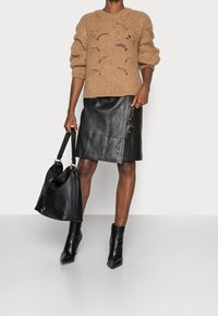 Pull beige en tricot avec des motifs ondulés texturés, associé à une jupe en cuir noire avec un détail à boutons, des bottines noires et un grand sac noir.