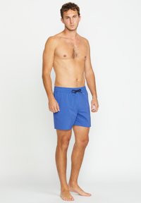 Shorts de bain bleus en tissu léger, avec une taille élastique dotée d'un cordon noir et des poches sur les côtés.