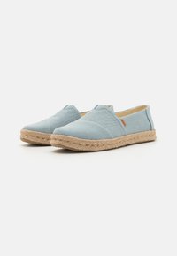 Lys blå kanvas slip-on sko med rund tå og flettet jutesåle. Har stikking detaljer og minimal merkevare på siden.