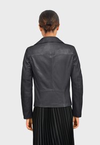 Čierna kožená bunda s klasickým golierom, štruktúrovanými švami a prispôsobeným strihom, doladená s plisovanou čiernou sukňou.