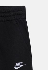 Pantaloni de trening negri cu talie elastică, având buzunare laterale și un logo Nike brodat alb în față. Țesătură moale și netedă.