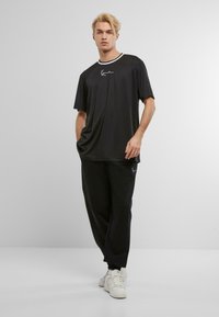 Svart T-skjorte med hvit stripet krage og brodert logo. Kombinert med løstsittende svarte joggebukser og hvite sneakers.
