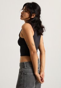 Top corto senza maniche di colore nero con design aderente, abbinato a jeans grigi a vita alta con tasche posteriori e cuciture a contrasto.