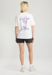 T-shirt en coton blanc avec un design graphique violet représentant un verre à cocktail et du texte au dos. Manches courtes et coupe décontractée.